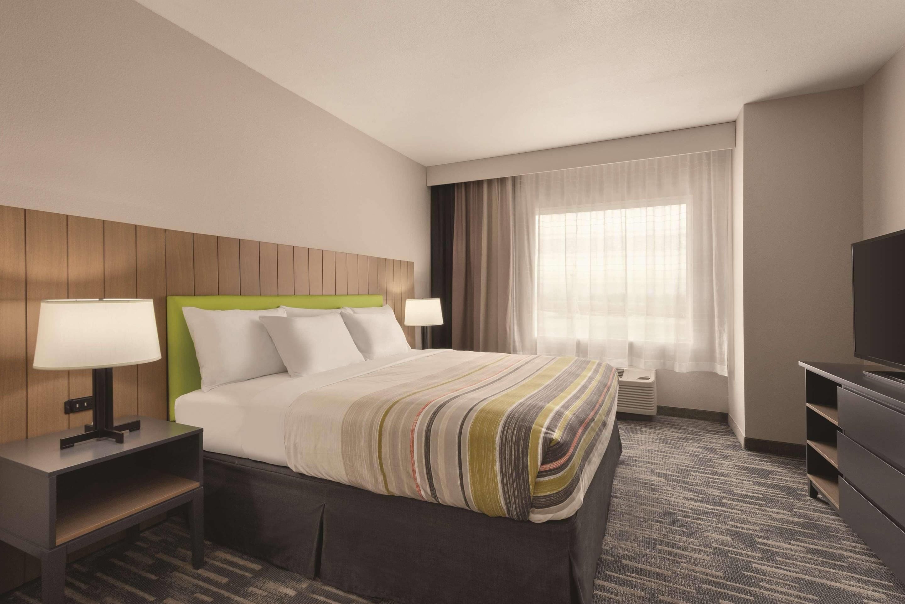 Ein Hotelzimmer mit Bett, Nachttischen, Fernseher, einem Fenster mit Vorhängen und Teppichboden.