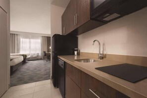 A compact hotel room with a kitchenette, a bed, a desk, and a window with curtains. - Country Inn & Suites by Radisson, Oklahoma City-Bricktown, OK (Oklahoma City)