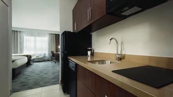 A compact hotel room with a kitchenette, a bed, and a view of the outdoors.