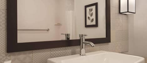 Un baño con un lavabo blanco, un espejo grande y una obra de arte con una hoja enmarcada en la pared.