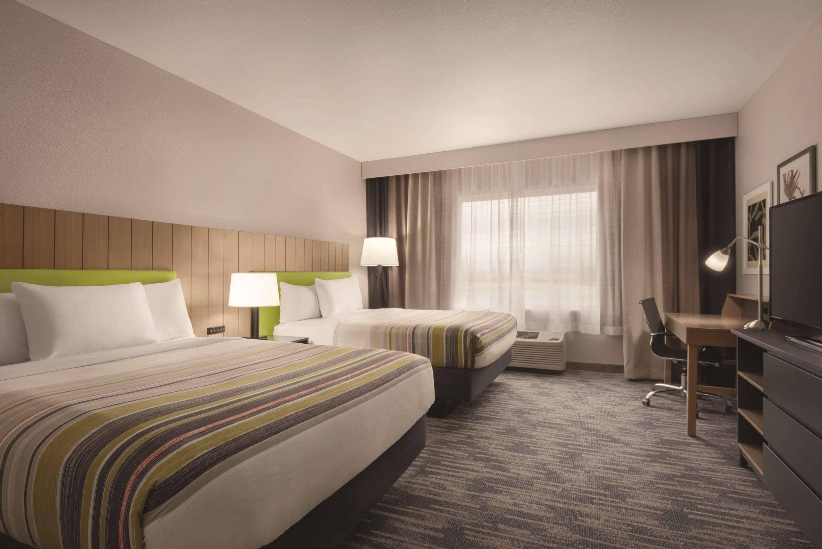 A hotel room with two beds, a desk, a chair, a TV, and a window with curtains.