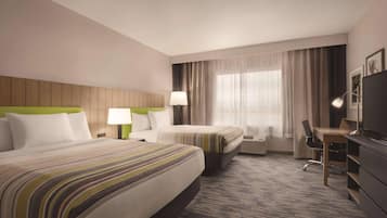 Quarto de hotel com duas camas, uma escrivaninha, uma cadeira, uma televisão e uma janela com cortinas.
