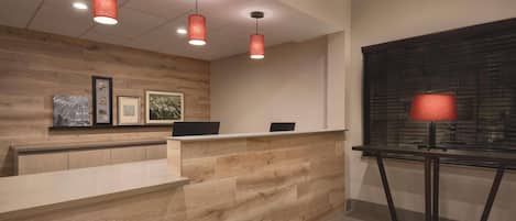 Un área de recepción con un mostrador de madera, tres lámparas colgantes y obras de arte enmarcadas en la pared.