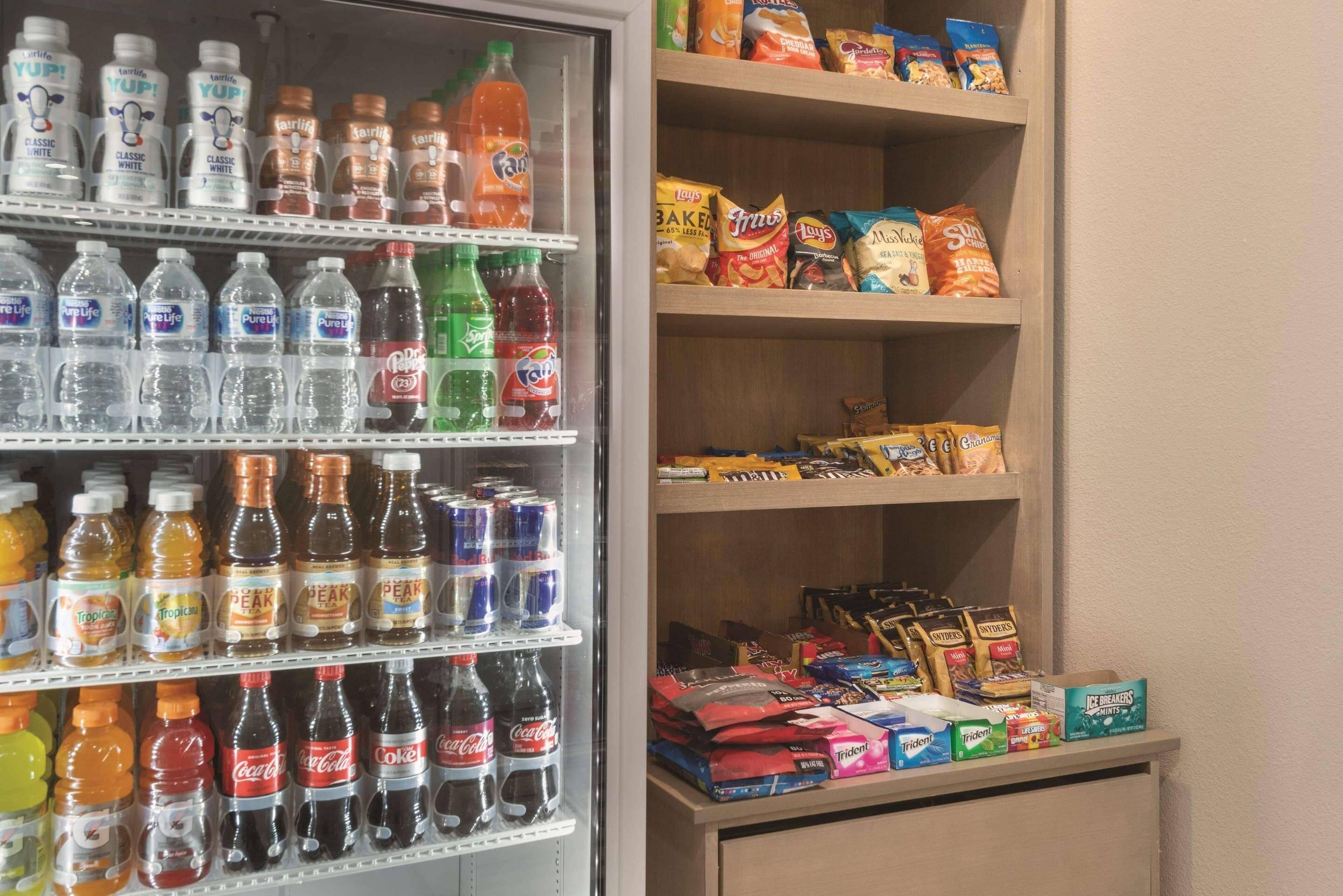 Un refrigerador lleno de bebidas variadas y un estante con aperitivos y helados.