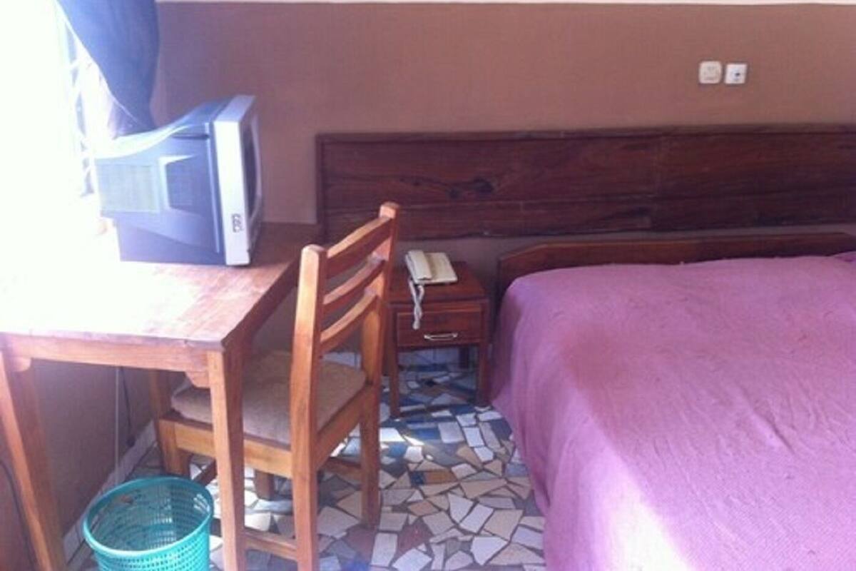 Una habitación con cama, escritorio, silla, televisión y teléfono.