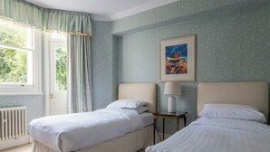 A room with two single beds, a radiator, a window with curtains, and a framed painting on the wall.