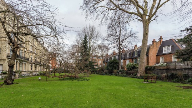 A residential area with a grassy lawn, trees, and houses with brick facades and pitched roofs.