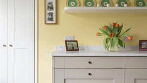A room with a white door, a white dresser with drawers, a vase with red flowers, and decorative plates on shelves.