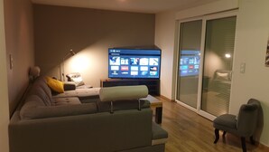 Un salon avec un canapé gris, un téléviseur et une porte-fenêtre coulissante.