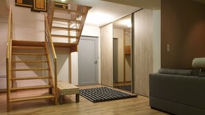 Une pièce avec un escalier en bois, un canapé gris et une porte qui donne sur une autre pièce.