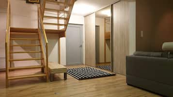 Une pièce avec un escalier en bois, un canapé gris et une porte qui donne sur une autre pièce.