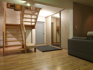 Une pièce avec un escalier en bois, un canapé gris et une porte qui donne sur une autre pièce.