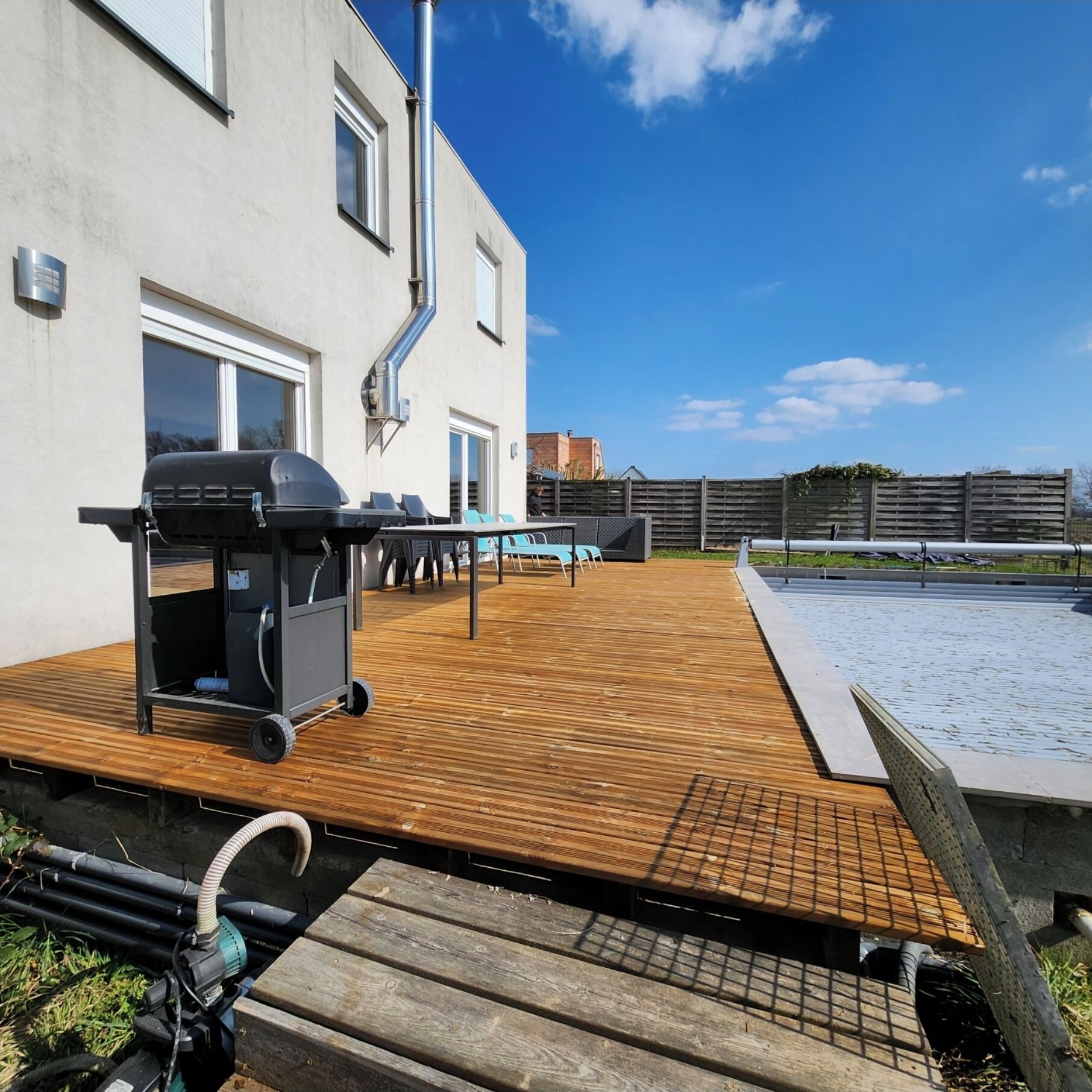 Une terrasse extérieure équipée d’un barbecue, d’une piscine et d’un sol en bois.