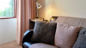 Ein Zimmer mit einer Ledersofa, einem Beistelltisch mit Lampe und einem Fenster mit Vorhängen.