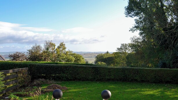 Ein gepflegter Garten mit Holzzaun, zwei kugelförmigen Polstern und Blick ins Grüne.