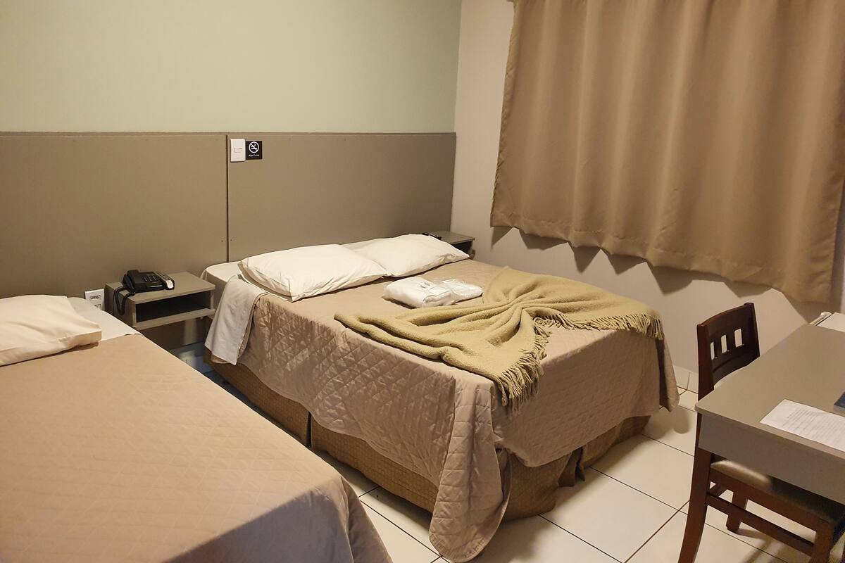 A hotel room with two beds, a desk, a chair, a telephone, and a curtain.