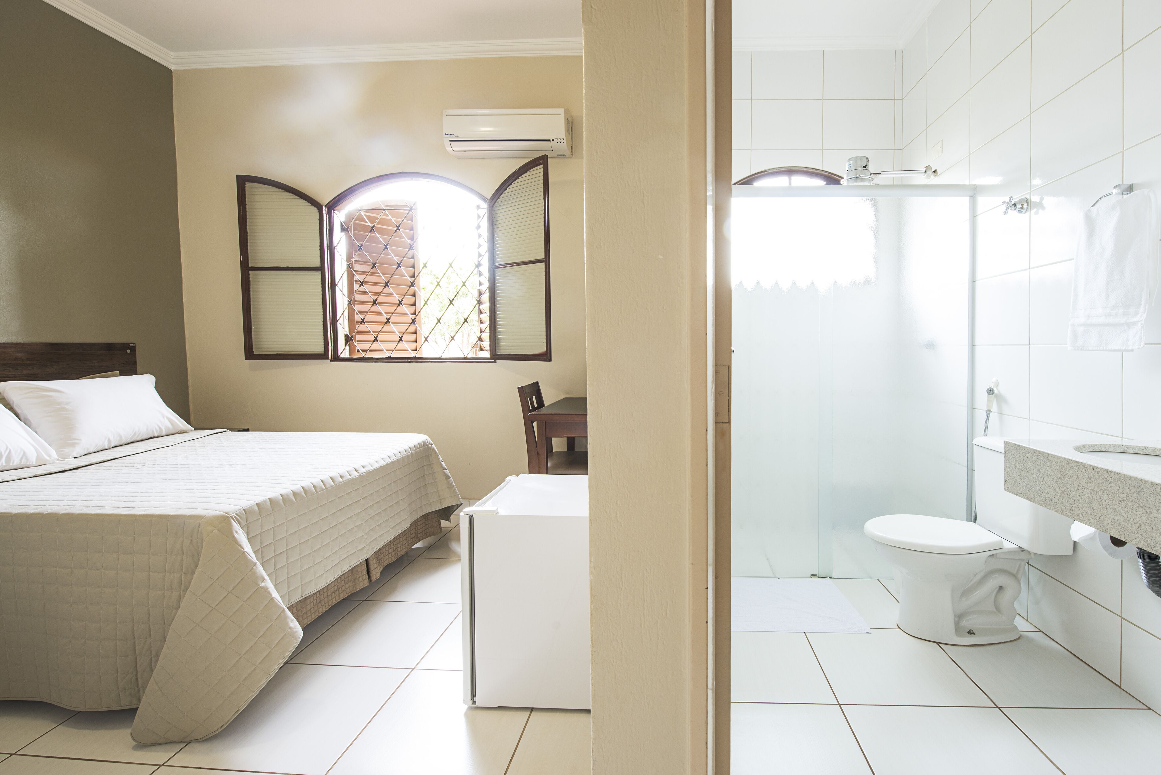 A bedroom with a bed, a window with blinds, and an air conditioning unit on the wall.