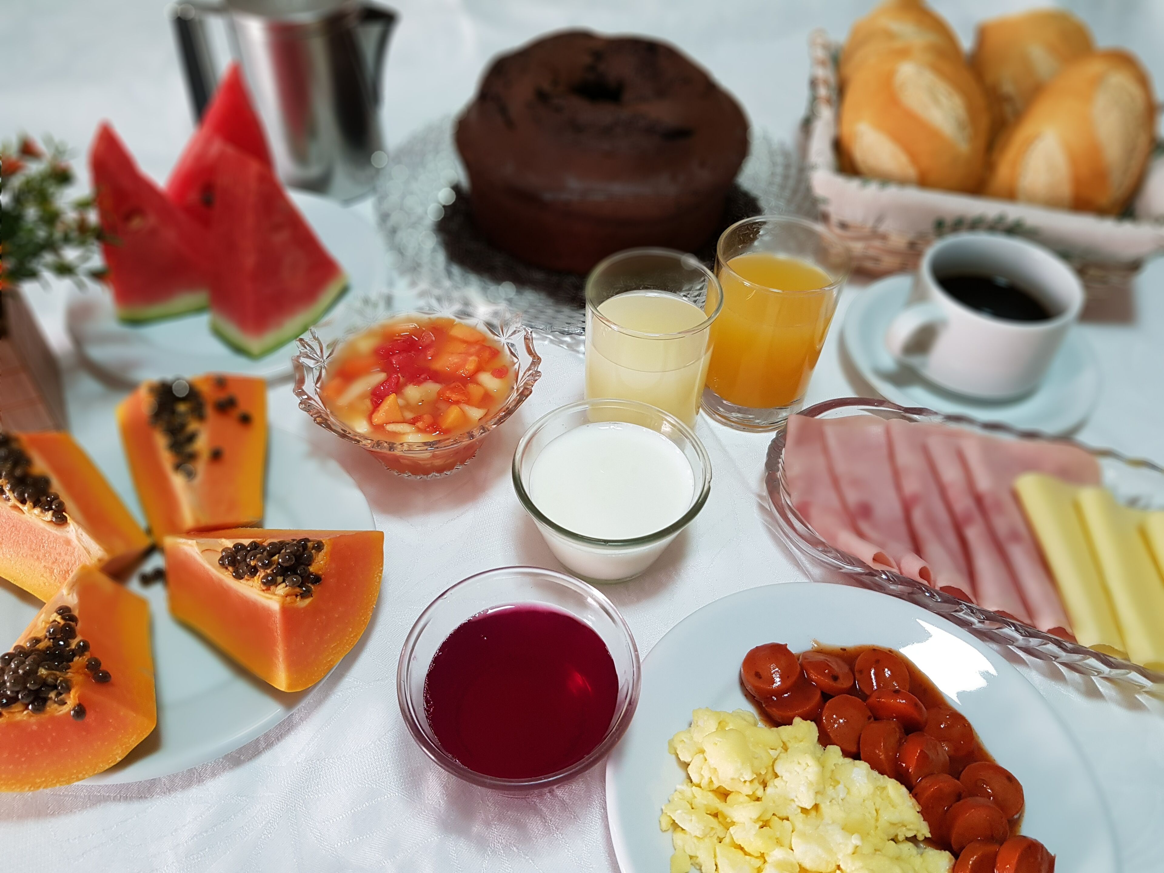 A breakfast table with various food items including eggs, sausages, ham, and pastries.
