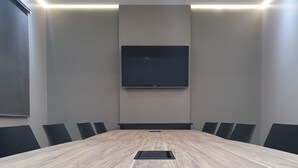 A conference room with a large wooden table, black chairs, a flat-screen TV mounted on the wall, and recessed ceiling lighting. - Hotel Recreio dos Bandeirantes (Sertaozinho)