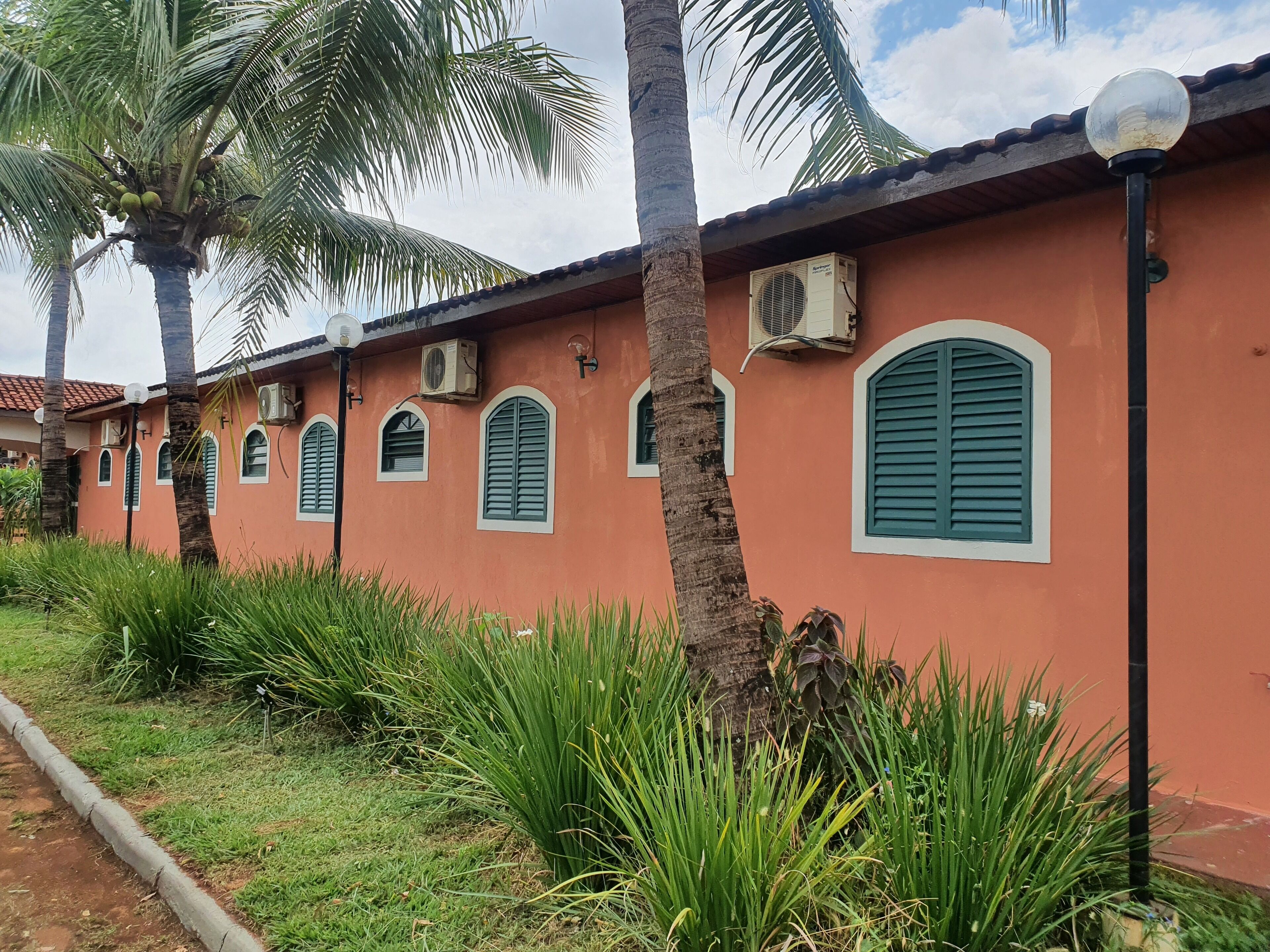 A row of buildings with arched windows and air conditioning units, surrounded by palm trees and greenery.