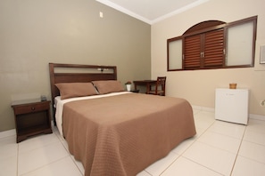 A bedroom with a bed, a nightstand, a chair, a small table, and a refrigerator. - Hotel Recreio dos Bandeirantes (Sertaozinho)