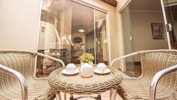 A wicker table with three white teapots and cups, a glass door leading to a balcony, and a framed picture on the wall. - Hotel Recreio dos Bandeirantes (Sertaozinho)