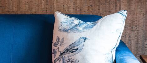 A blue sofa with a decorative pillow featuring a bird and floral design, positioned against a textured wall.