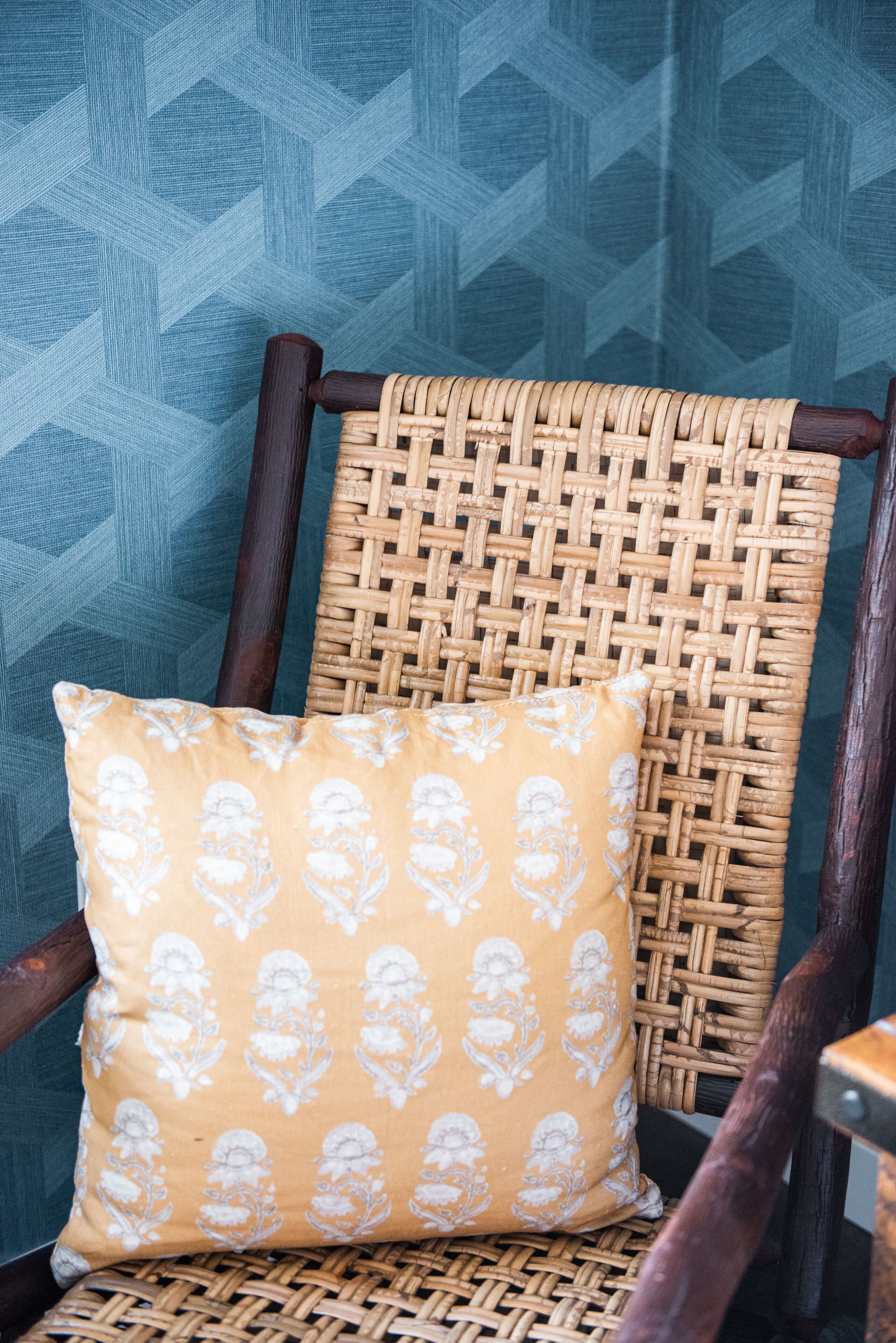 A wicker chair with a cushion against a patterned wall.