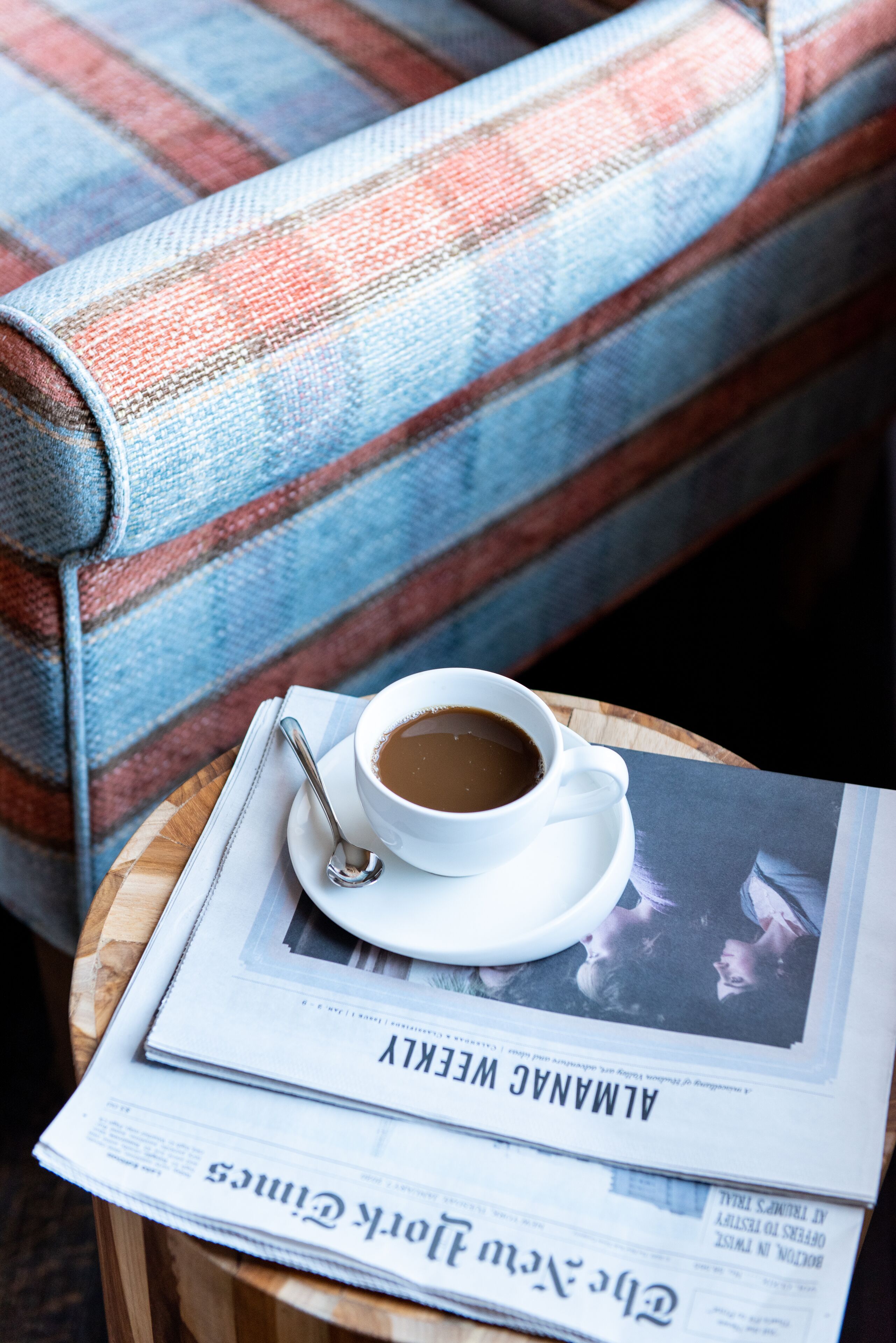 Une tasse de café posée sur une soucoupe, une cuillère et un journal sur une petite table ronde.