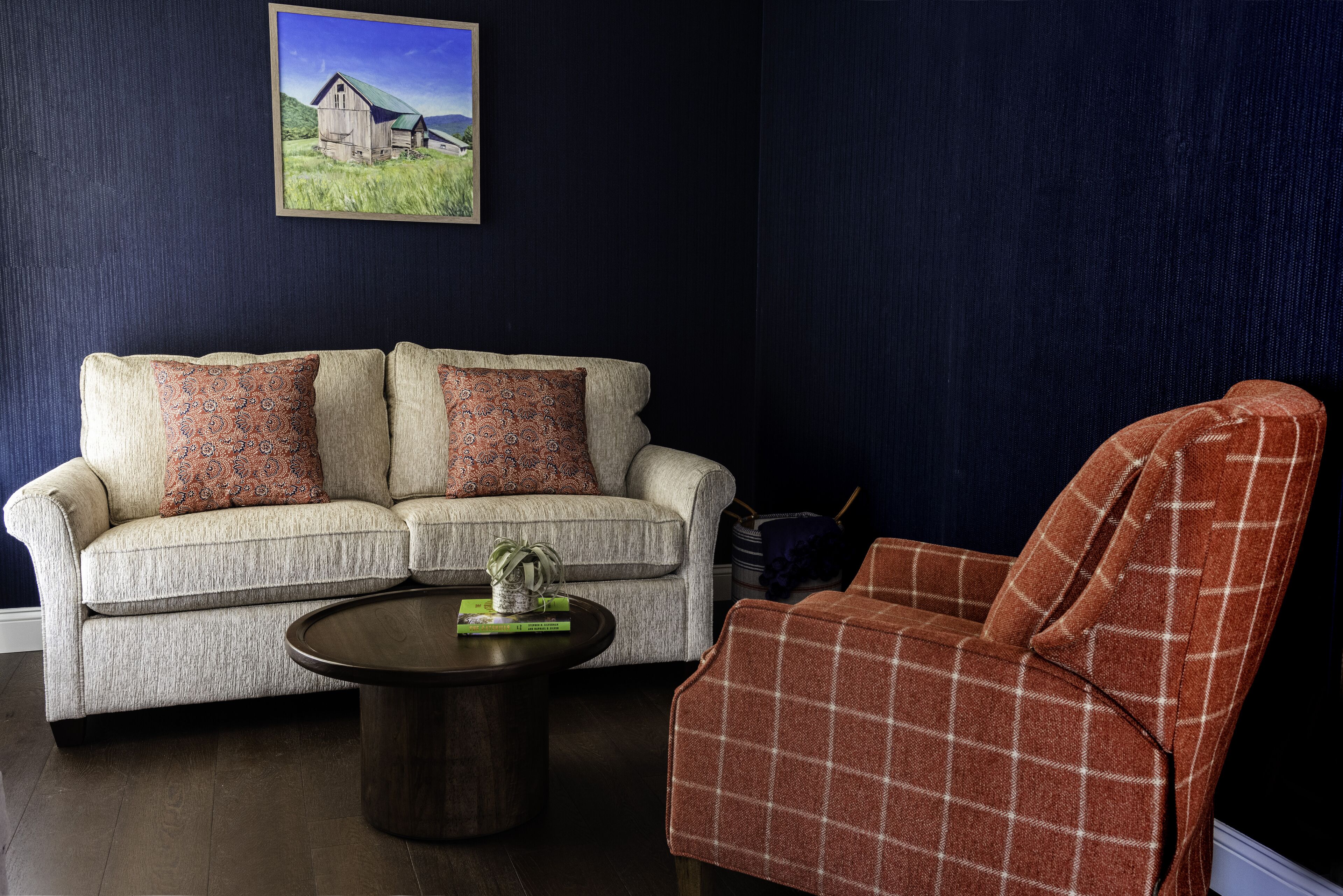 A living room with a sofa, armchair, coffee table, and a painting on the wall.