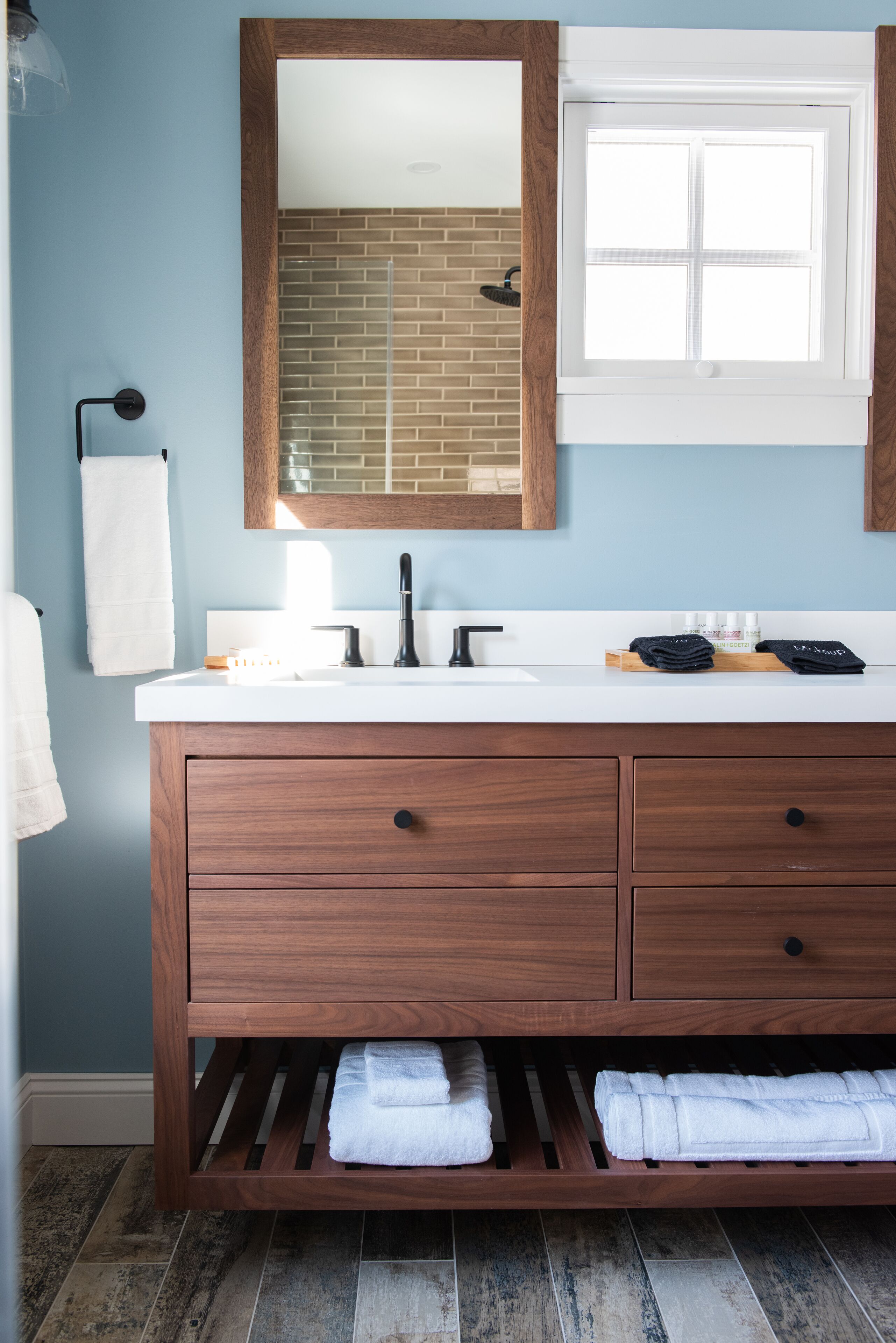 A bathroom with a wooden vanity, a white sink, a mirror, and a window.