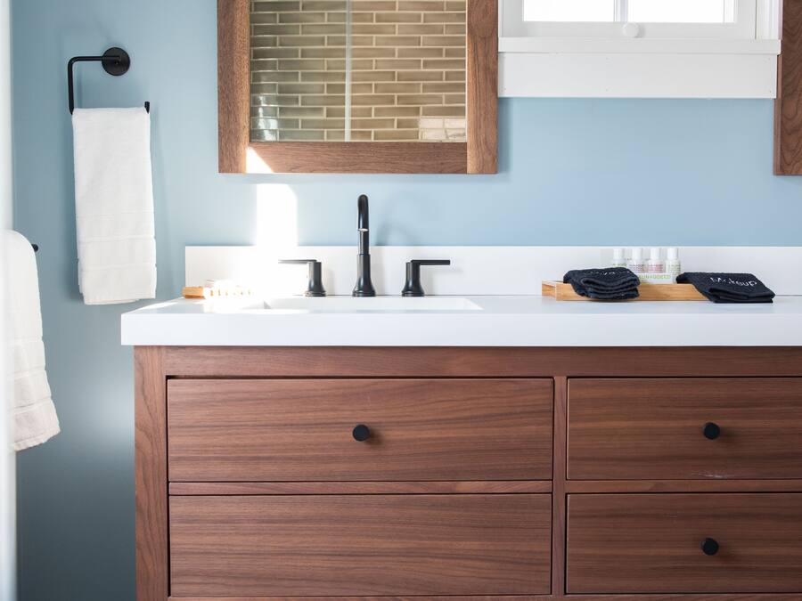 A bathroom with a wooden vanity, a white sink, a mirror, and a window.