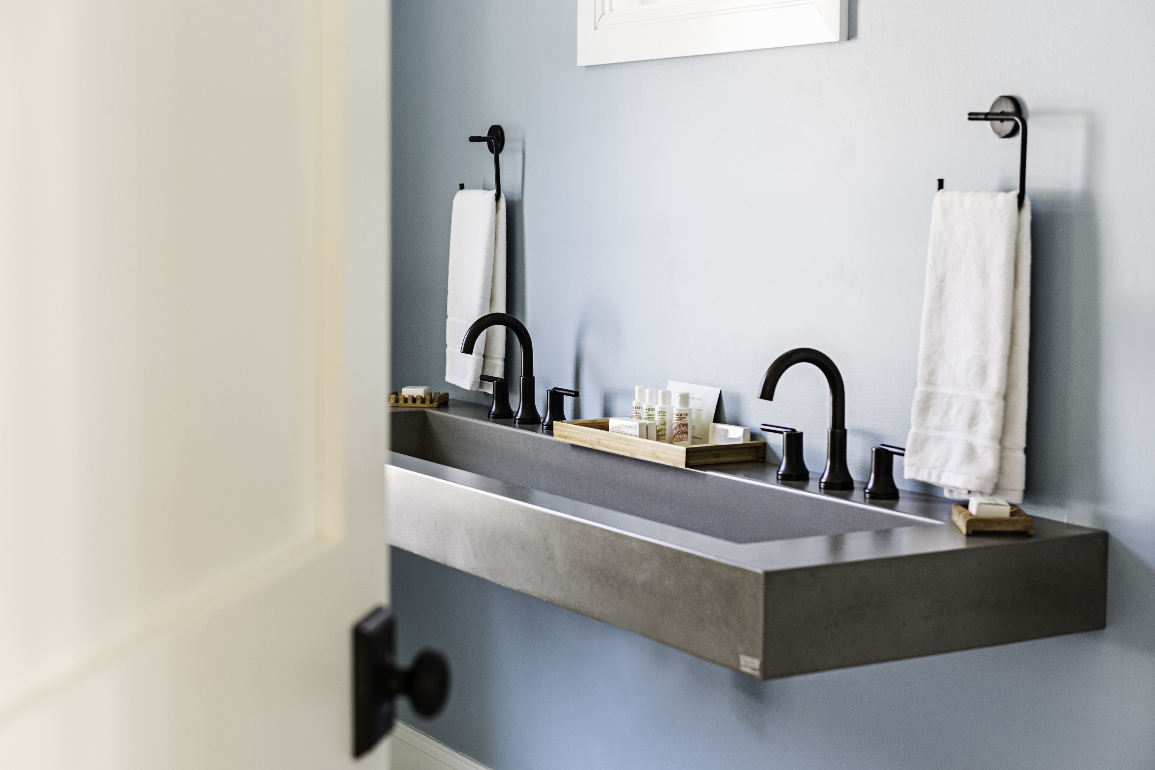 A bathroom with a large, rectangular sink, two black faucets, and two white towels hanging on towel racks.