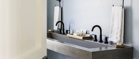 A bathroom with a large, rectangular sink, two black faucets, and two white towels hanging on towel racks.