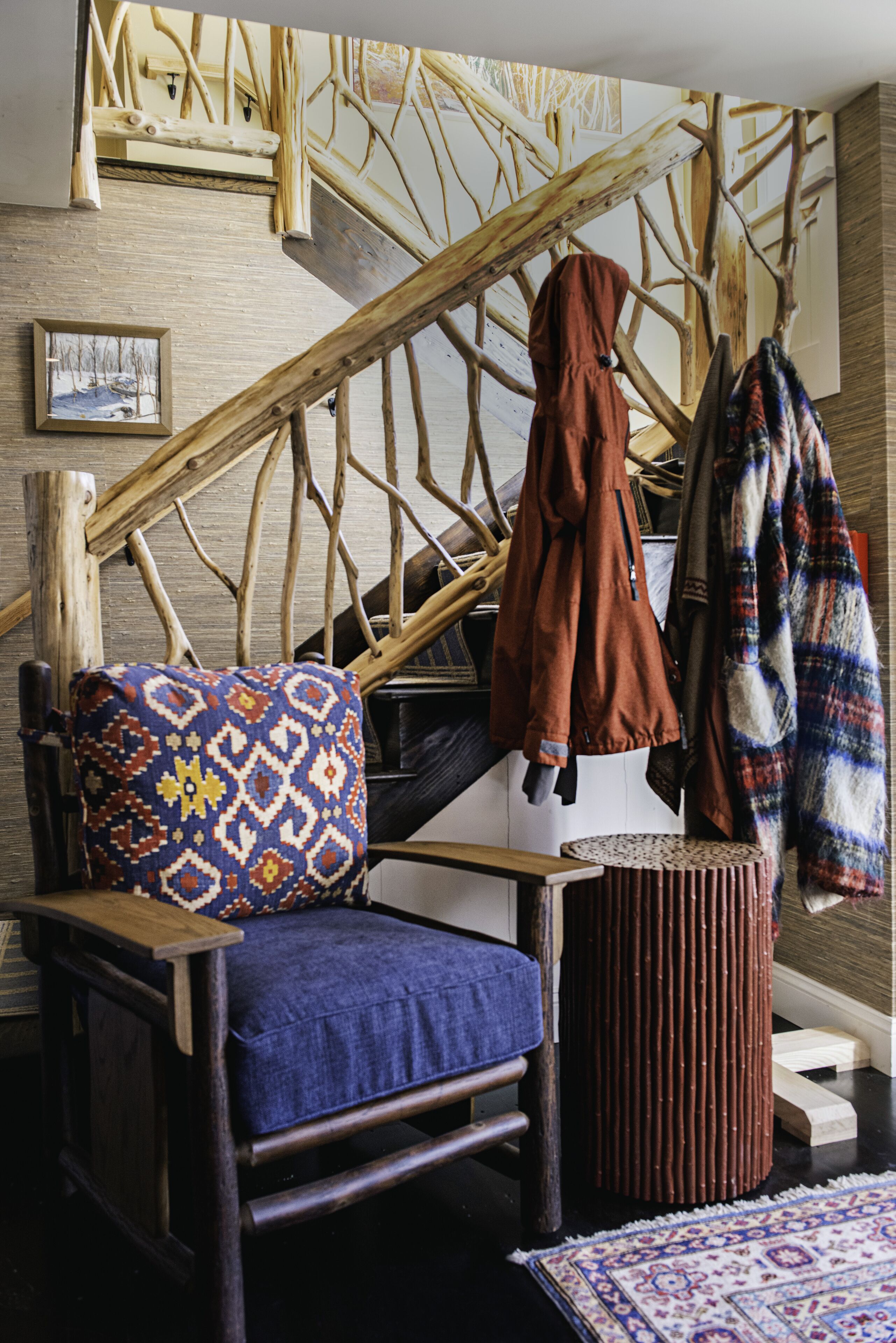 A wooden chair with a patterned cushion, a small round stool, and a staircase with wooden railings.