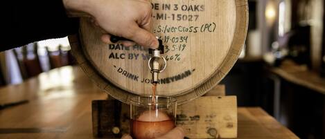 Una mano vertiendo cerveza desde un grifo de barril de madera con la etiqueta 'Journeyman Distiller' en un vaso.