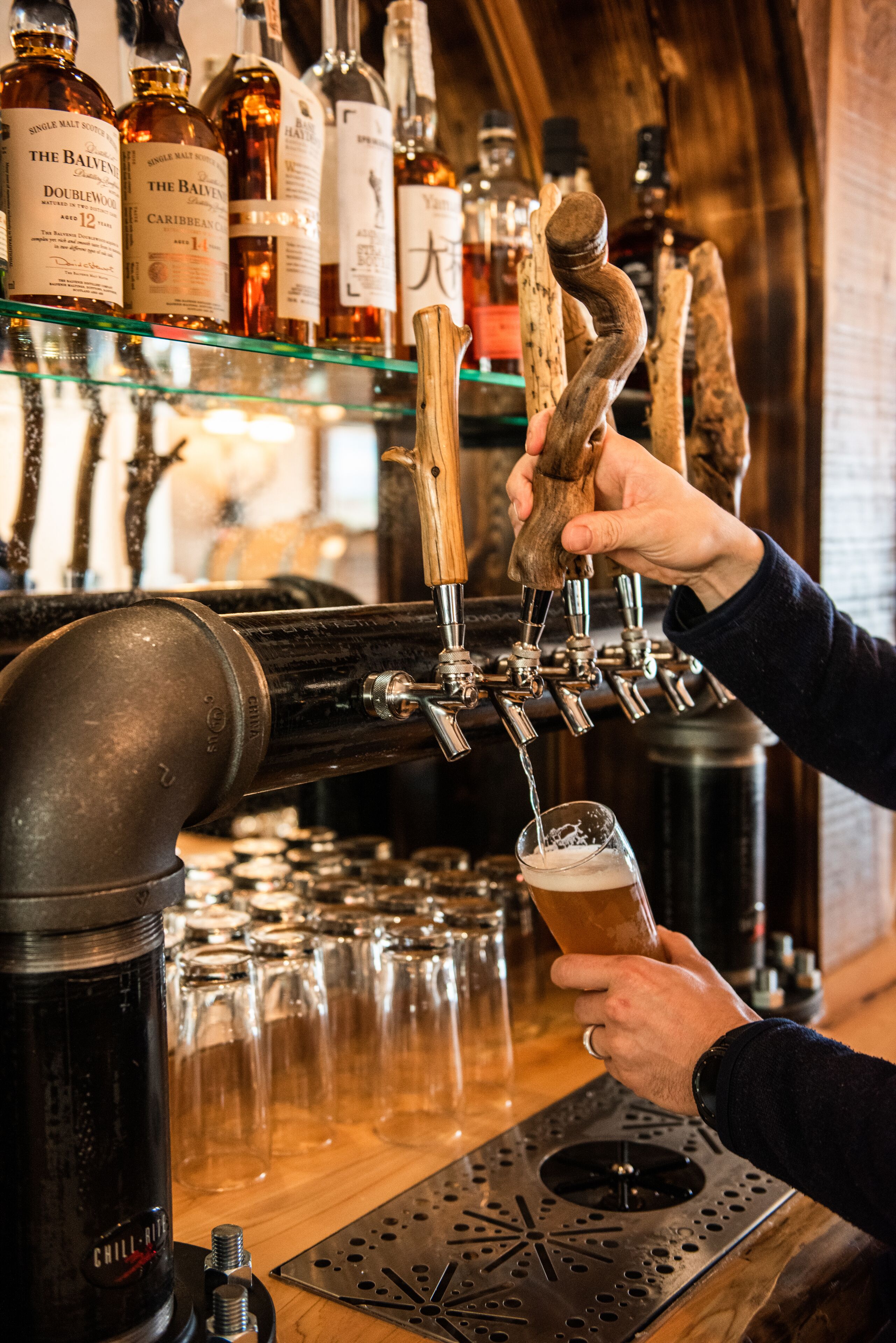 A bar with multiple taps and bottles, a person pouring a drink, and glasses lined up on the counter.