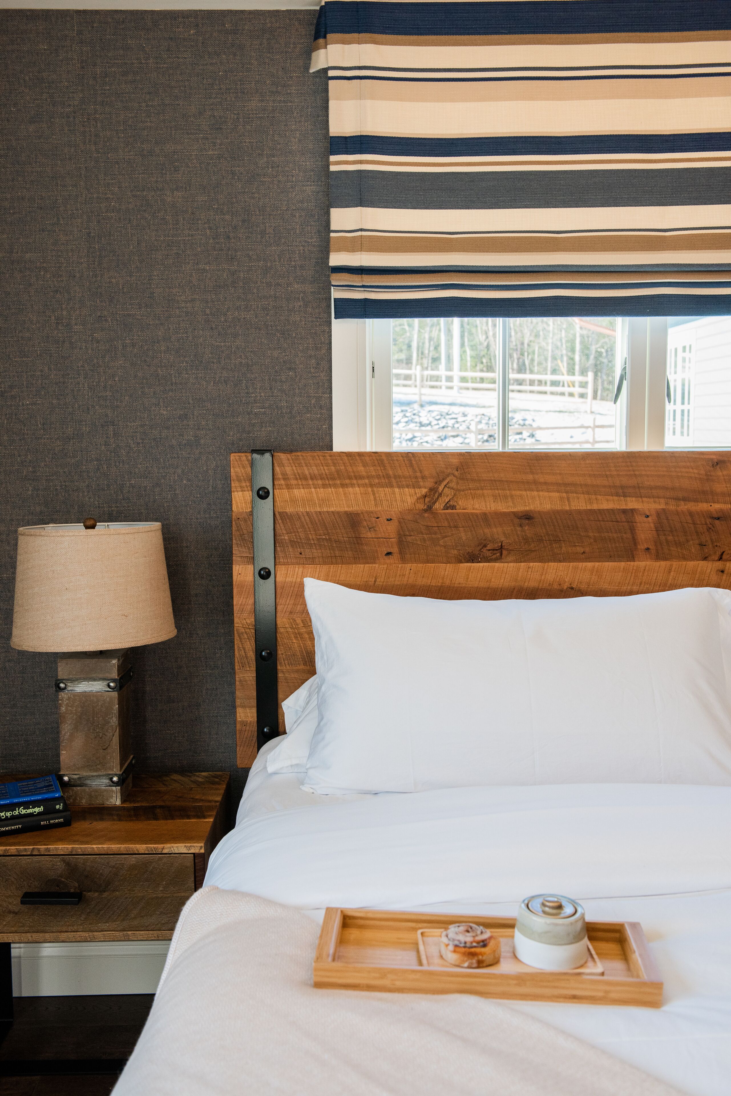 A neatly made bed with white linens, a wooden headboard, and a bedside table with a lamp and books.