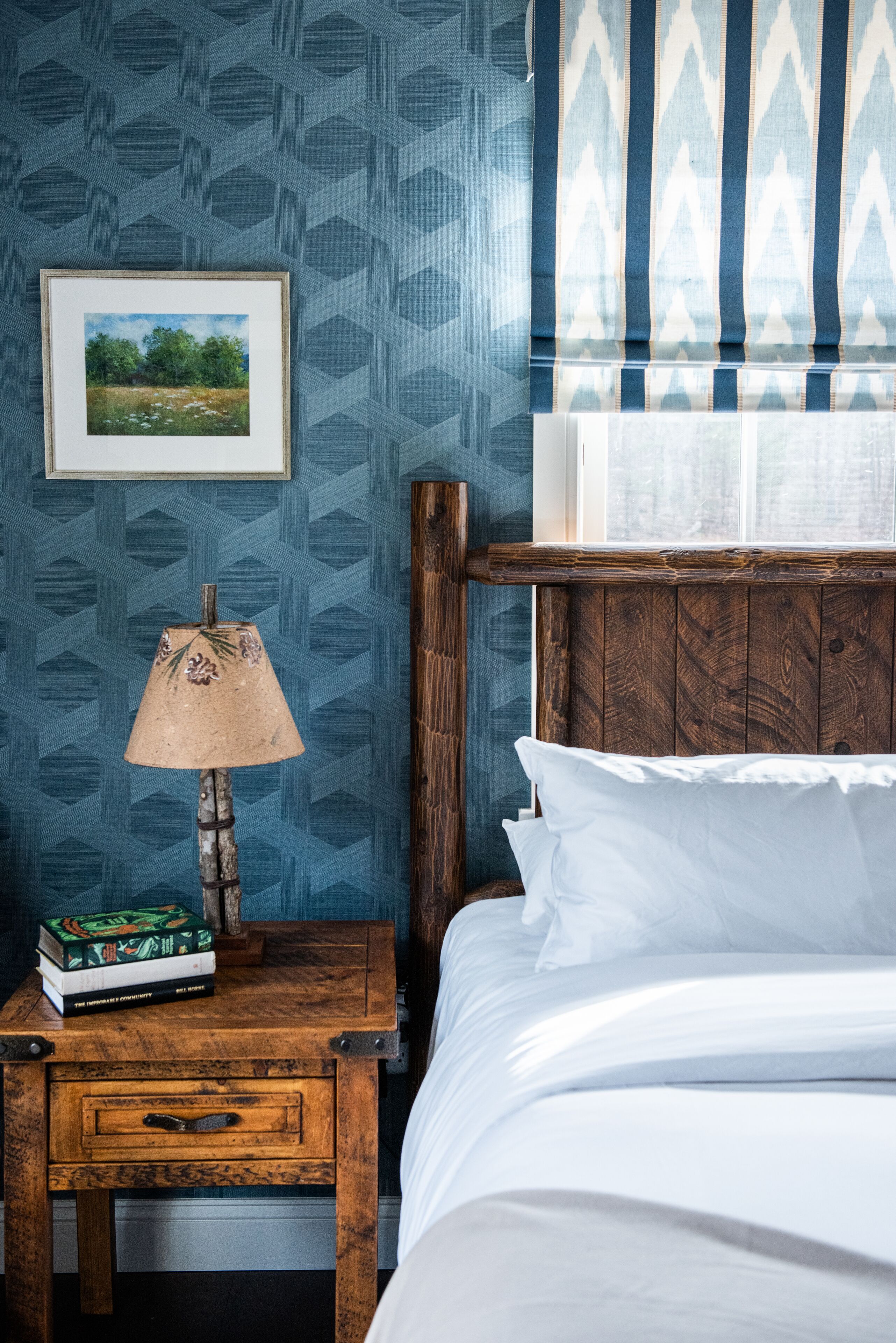 A bedroom with a wooden headboard, a nightstand with a lamp and books, and a framed picture on the wall.