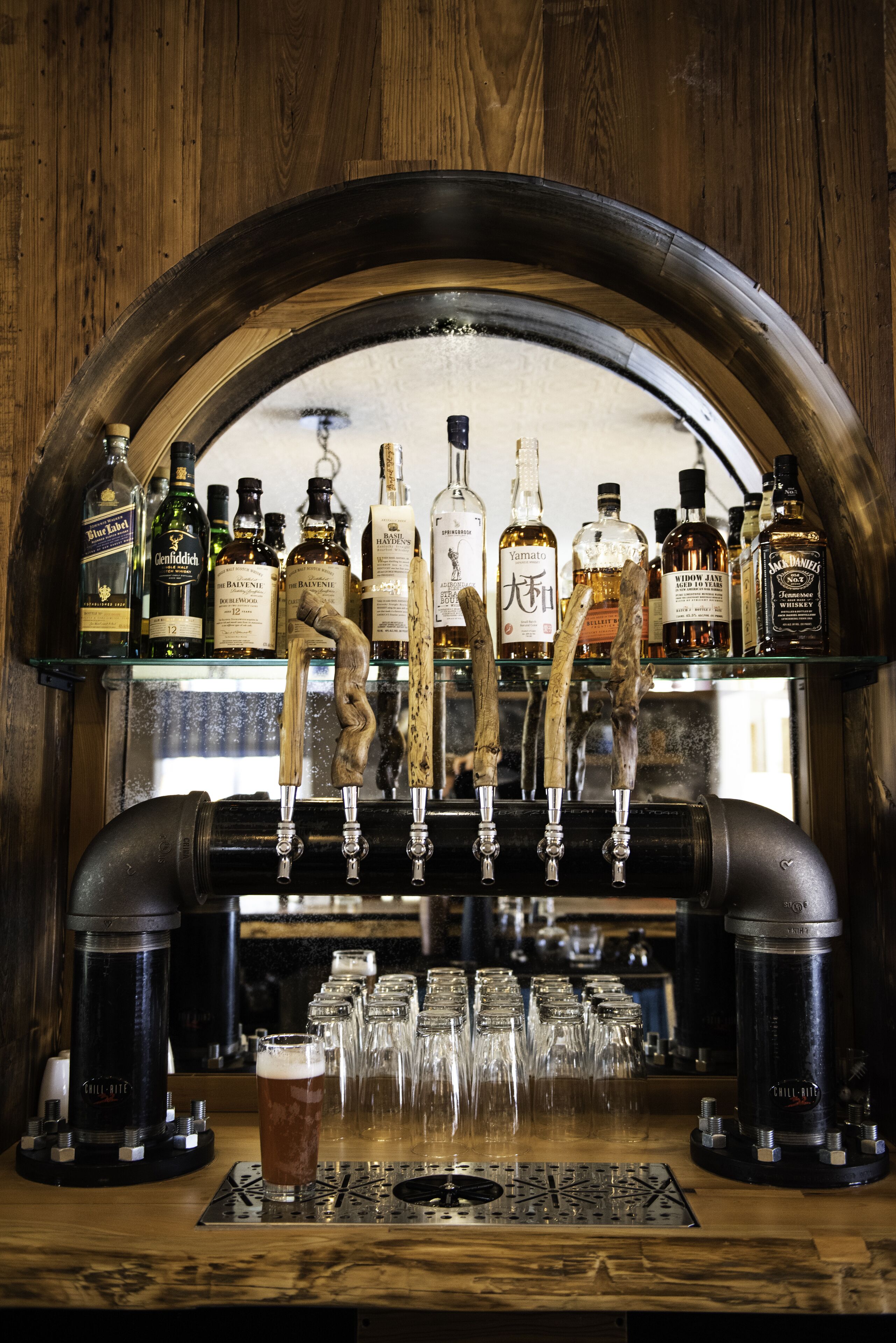 A bar with a wooden backdrop, multiple liquor bottles, and a tap system.