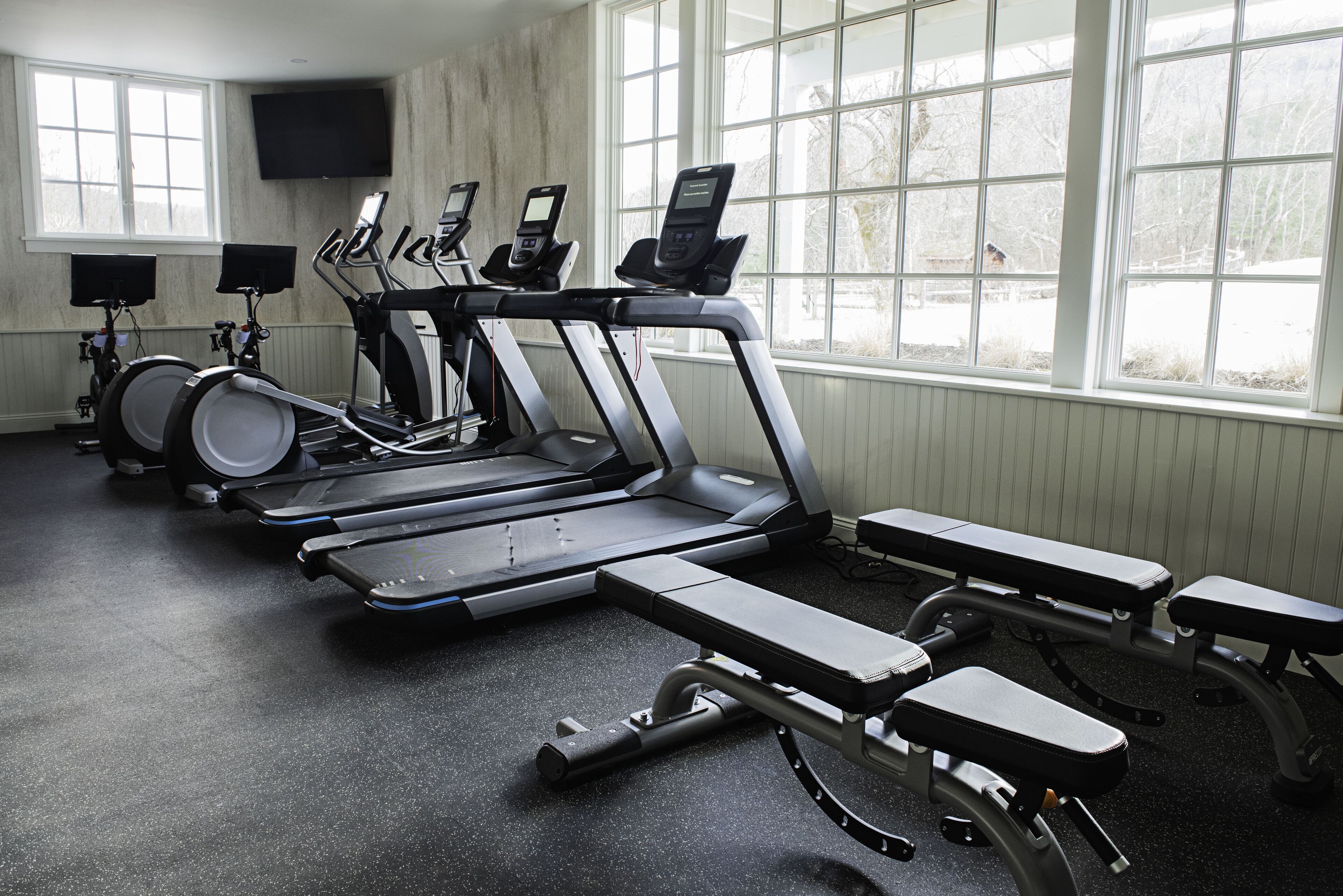 Un gimnasio con cintas de correr, elípticas y una banca.