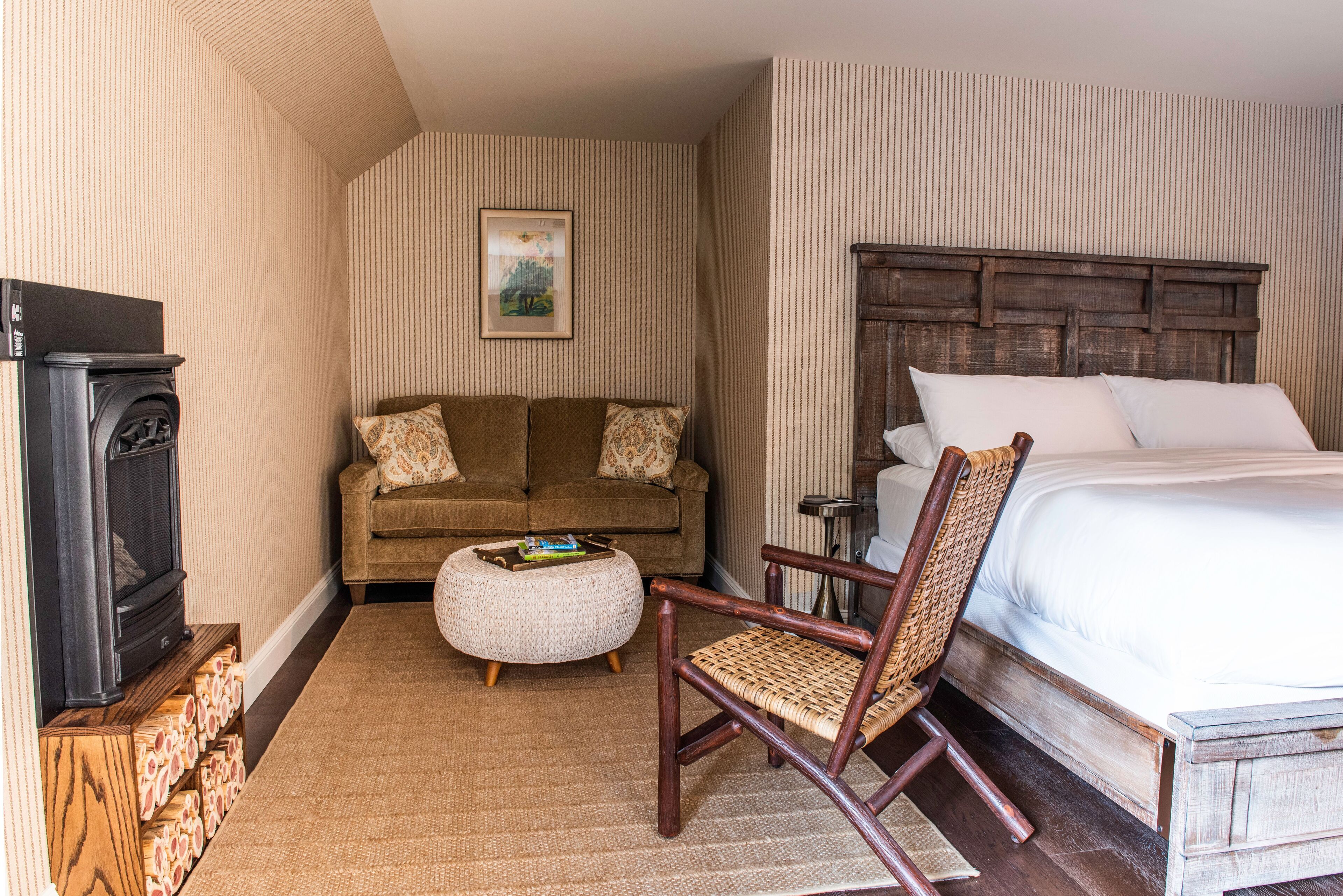 A hotel room with a bed, a sofa, a chair, a small table, and a fireplace.