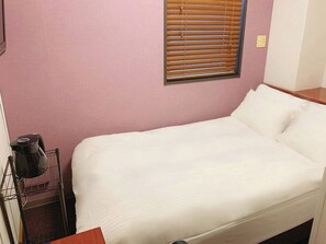 Una cama individual con ropa de cama blanca, cabecera de madera y una ventana con persianas.