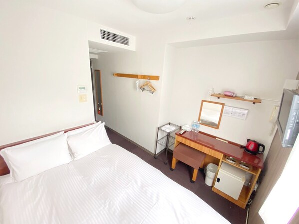 Habitación de hotel con cama, escritorio, espejo, televisor y un pequeño armario.
