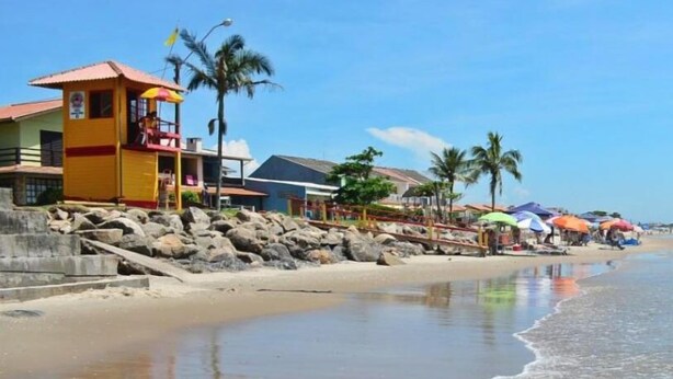 Una playa con una torre de salvavidas, palmeras y sombrillas.