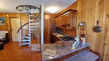Une cuisine avec des meubles en bois, un plan de travail en granit, une cuisinière encastrée et un escalier en colimaçon menant à une autre pièce.