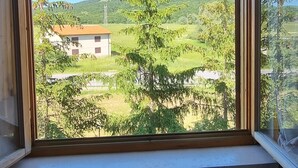 Une pièce dotée d’une grande fenêtre donnant sur un paysage rural, avec une maison et des arbres.