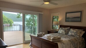 A bedroom with a wooden bed, a nightstand, a lamp, and a view of a balcony with a railing.