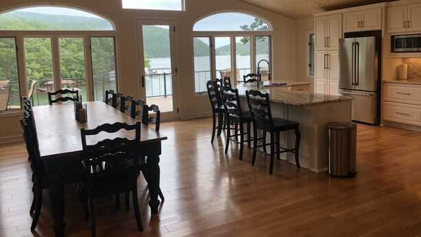 A spacious kitchen with wooden flooring, large windows, and a view of a lake.