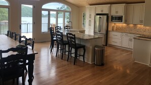 A spacious kitchen with wooden flooring, white cabinets, a stainless steel refrigerator, and a large island with seating.
